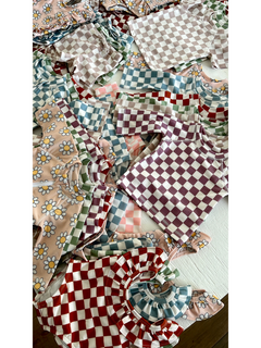 Colorful children's clothing featuring floral and checkered patterns, including tops and blouses stacked together.