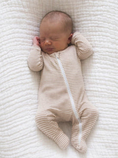 Newborn baby sleeping peacefully on a soft, textured blanket, wearing a striped zip-up onesie.