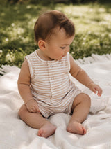 Baby wearing a striped onesie sits on a textured blanket in a grassy outdoor setting, absorbed in play.