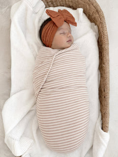 Newborn wrapped in a striped blanket, peacefully sleeping in a cozy basket with a soft knit blanket.