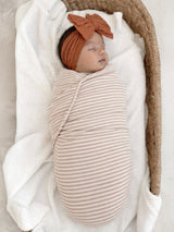 Newborn wrapped in a striped blanket, peacefully sleeping in a cozy basket with a soft knit blanket.