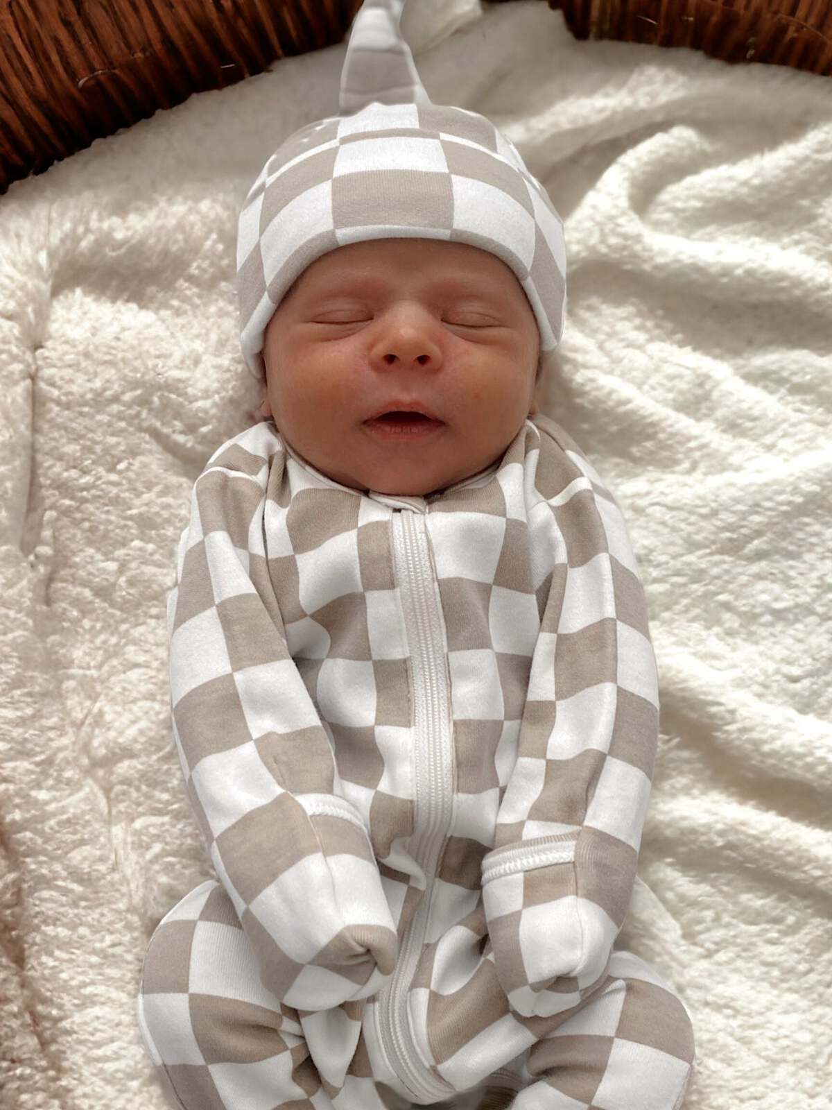 Newborn baby in a beige and white checkered outfit, peacefully sleeping on a soft blanket.