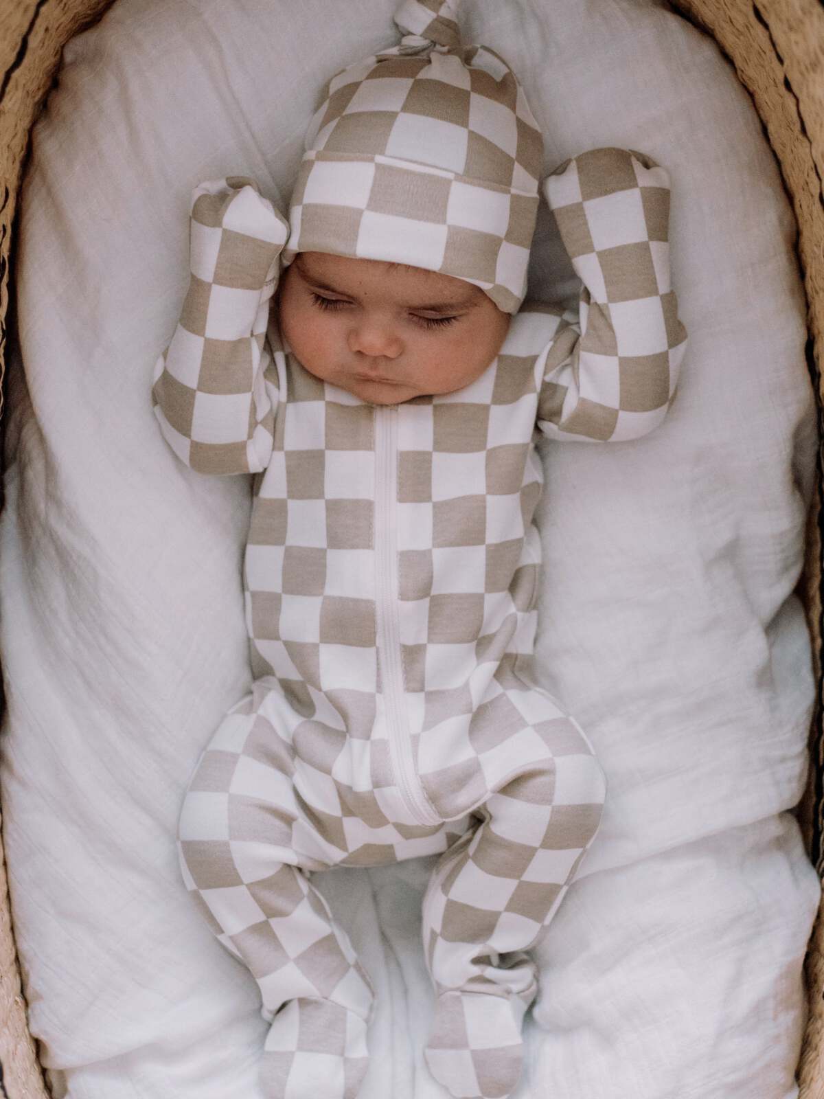 Infant in a beige and white checkered outfit lying on a soft blanket, looking peacefully asleep.