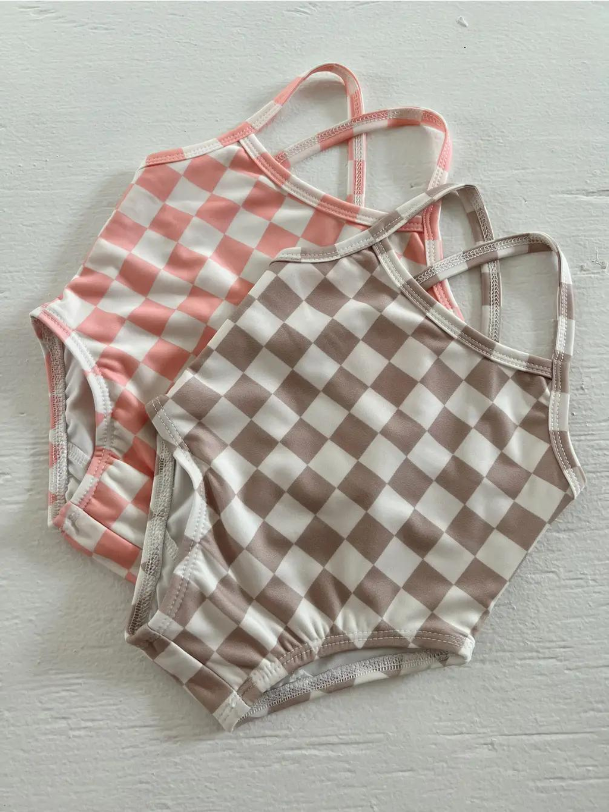 Two checkered swimsuits in peach and brown on a light background. Perfect for summer fun and stylish beach outings.